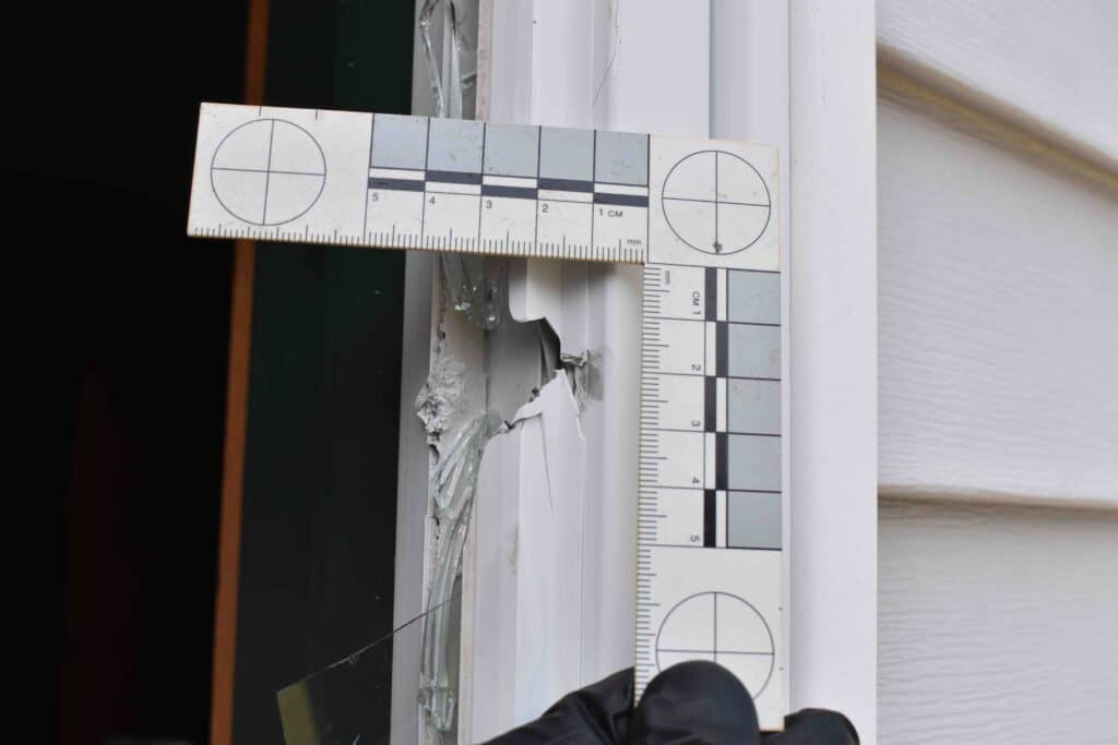 A Groton Criminal Investigator holds a tool up to a bullet hole in a door frame.