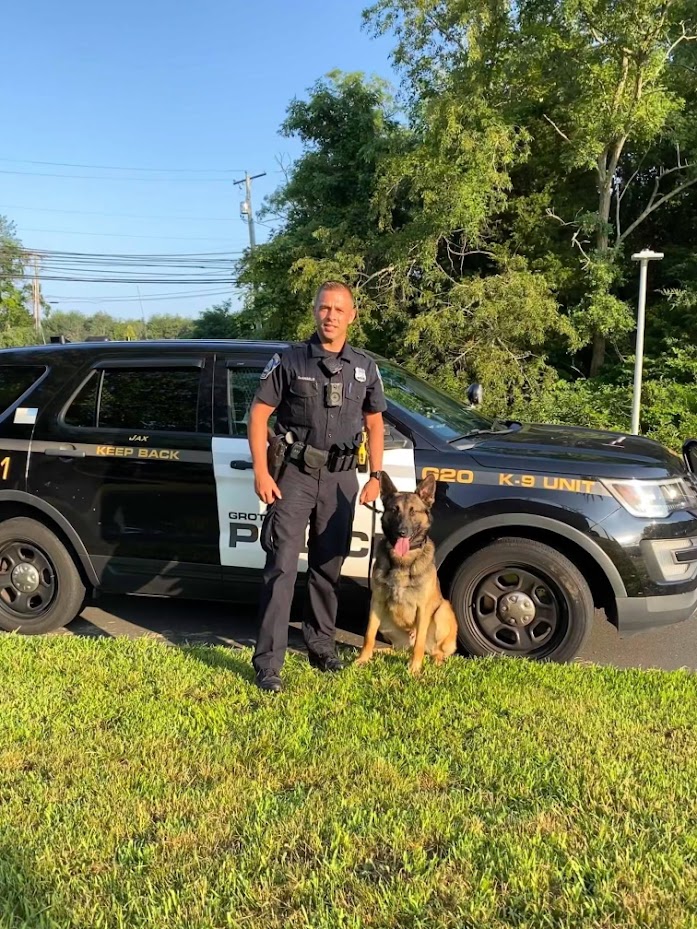 Groton Police Officer with a department K9 in front of a police cruiser.